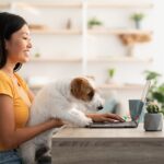 Pretty chinese lady freelancer working from home, petting her dog