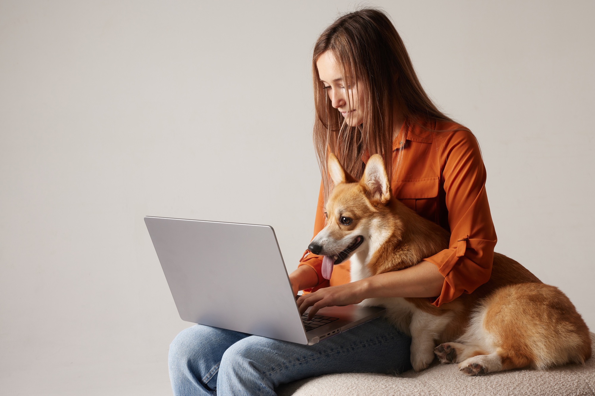 Woman working on laptop with Corgi dog on lap, cozy remote work lifestyle.
